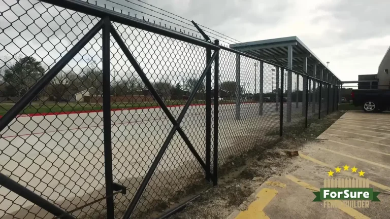 Black chain link commercial fence with barbed wire along a parking area