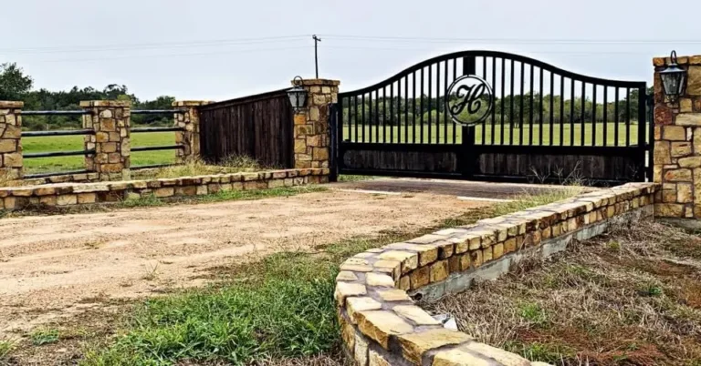 Arched iron estate entry gate with a monogram, set between stone columns